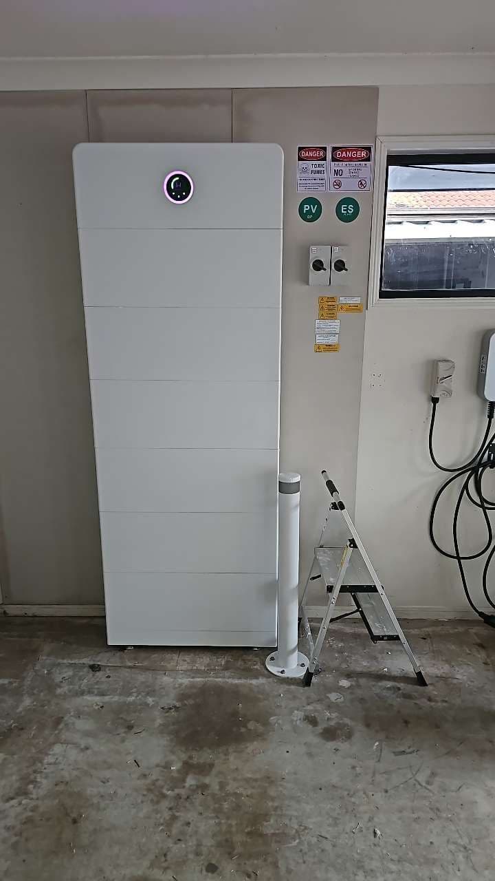 Modular battery installed in a garage beside an EV charger, with compliance signage