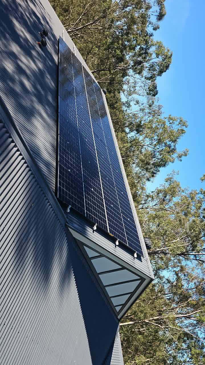 Solar panels on a dark Colorbond roof surrounded by gum trees