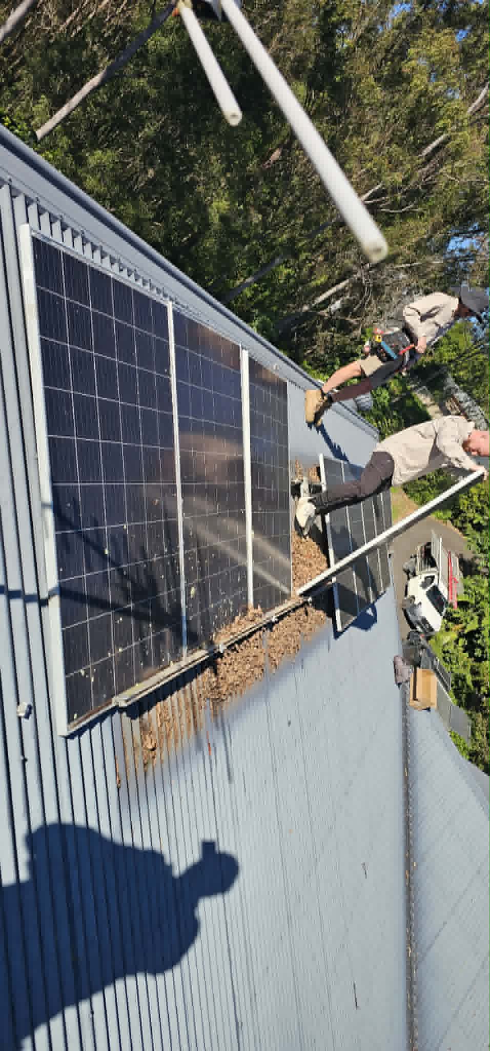Two installers lifting solar panels into place on a corrugated iron roof