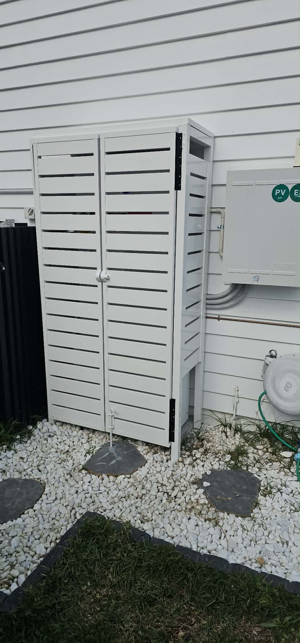 White slatted equipment enclosure beside a PV and energy storage labelled switchboard